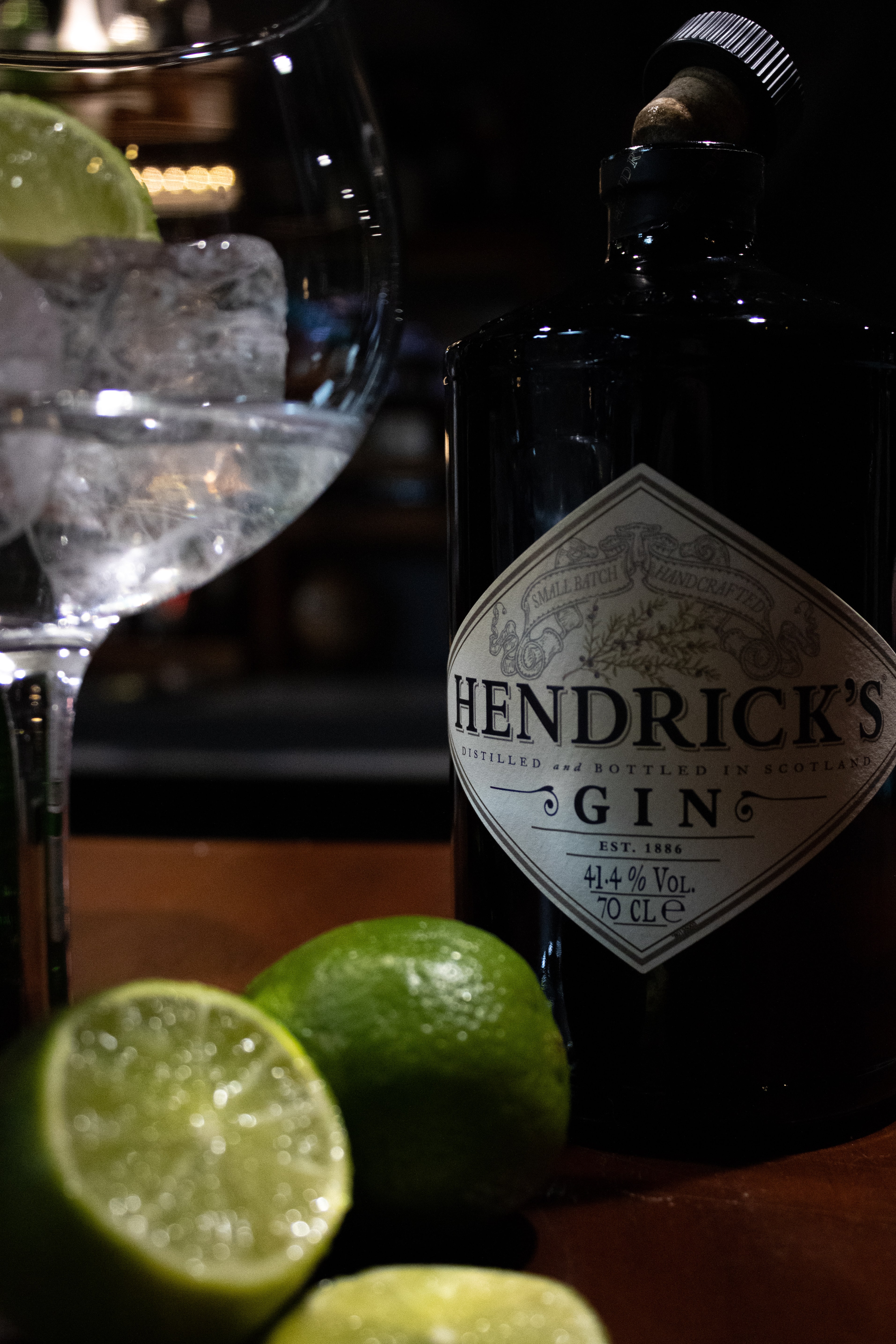 close up photograph of a bottle of hendrix gin next to a glass filled with tonic and ice and limes on the side